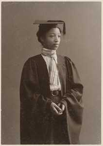 A black-and-white photo of a black woman in a graduate cap and gown.