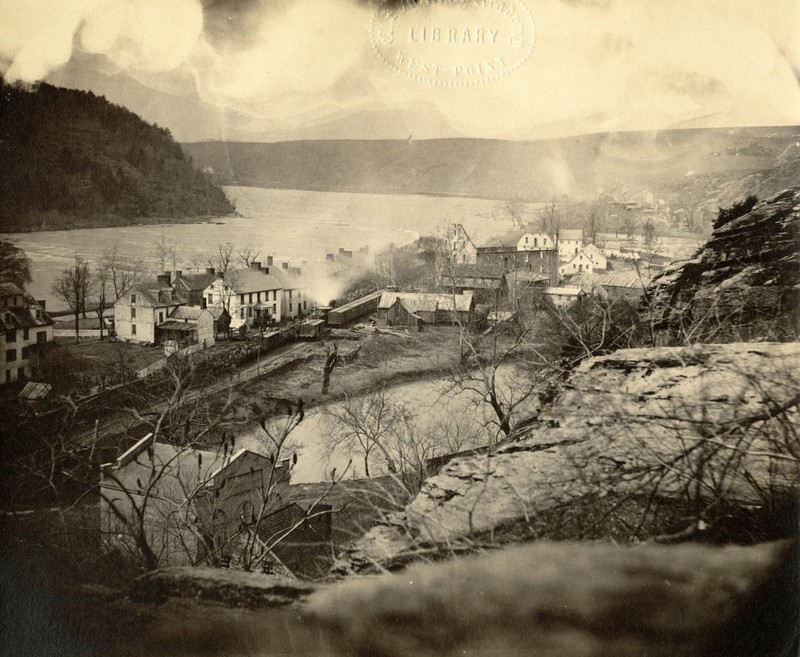 This photograph shows an 1864 view of Harpers Ferry from Jefferson Rock. A train carrying Union soldiers passes across Virginius Island. Courtesy of Crossroads of War.