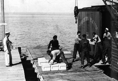 A white officer supervises African American enlisted men as they load munitions onto a vessel at Port Chicago. 
