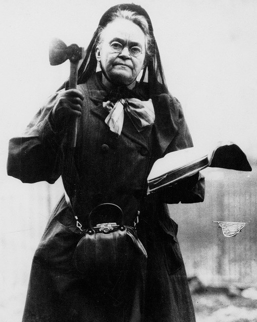 Carrie A. Nation in 1910, holding one of her hatchets in one hand and the Bible in another, a fitting depiction of her preference for virtue and the willingness to use violence if necessary to procure it.