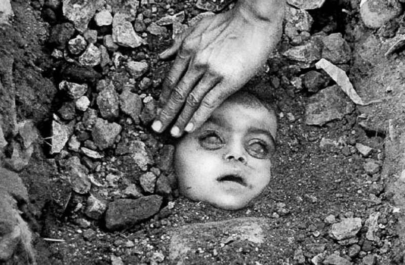 The face of a freshly buried child in Bhopal, India, victim of Carbide's disastrous chemical spill in 1984. Over 25,000 people died from direct effects of the fatal chemicals, and 150,000 continue to suffer health problems. Photo by Raghu Rai.