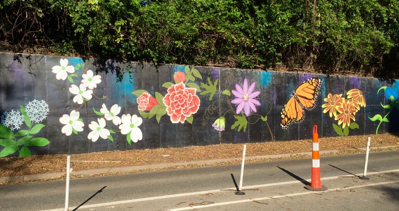 Along row of different, colorful flowers are painted on a black retaining wall.