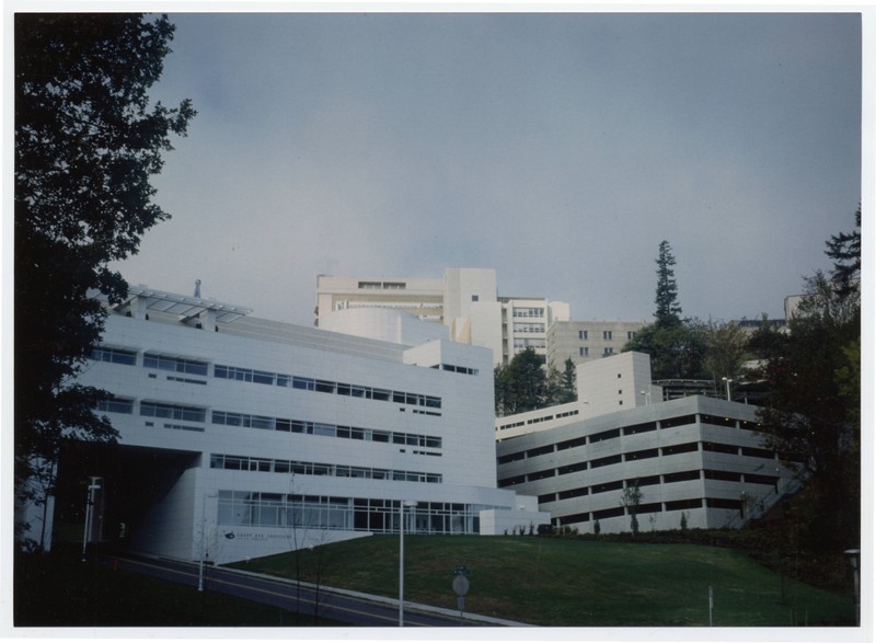 Color photograph of the exterior of the Casey Eye Institute, a white, modernist building situated in a canyon among other buildings.