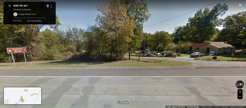 A colored photo of a paved and gravel road, with a house and sign nearby.