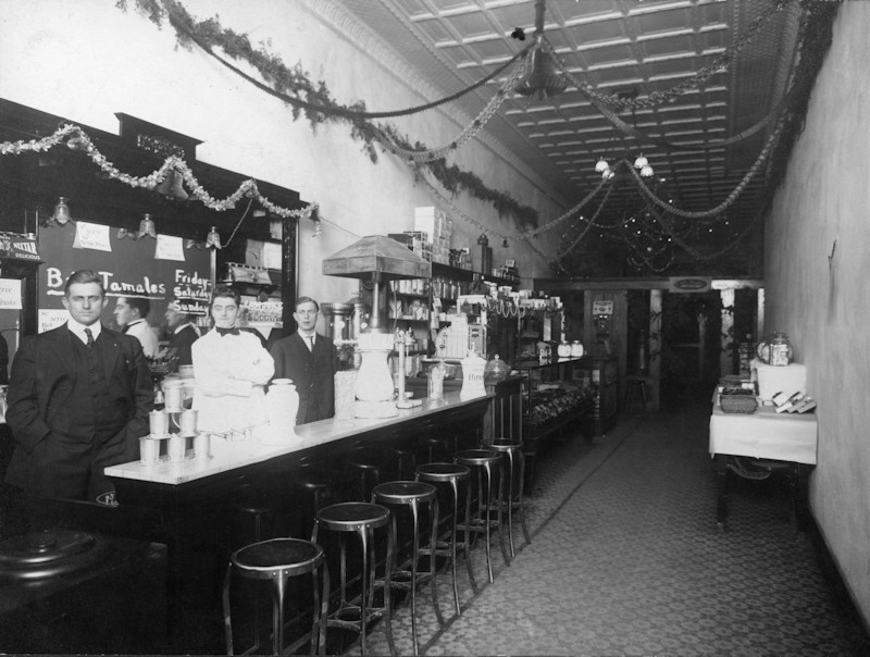 men stand behind the soda fountain counter