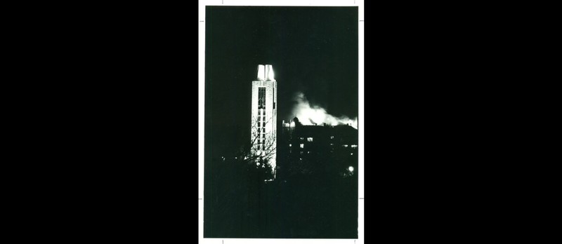 The Campanile stands in the foreground of the photograph while smoke and flames rise from the Union in the background.