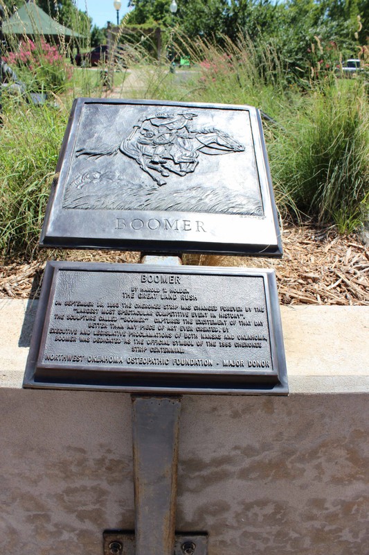 Bronze plaque with a relief image of a man on horseback, holding claim stakes in his hand. Another plaque below it has text explaining the image.