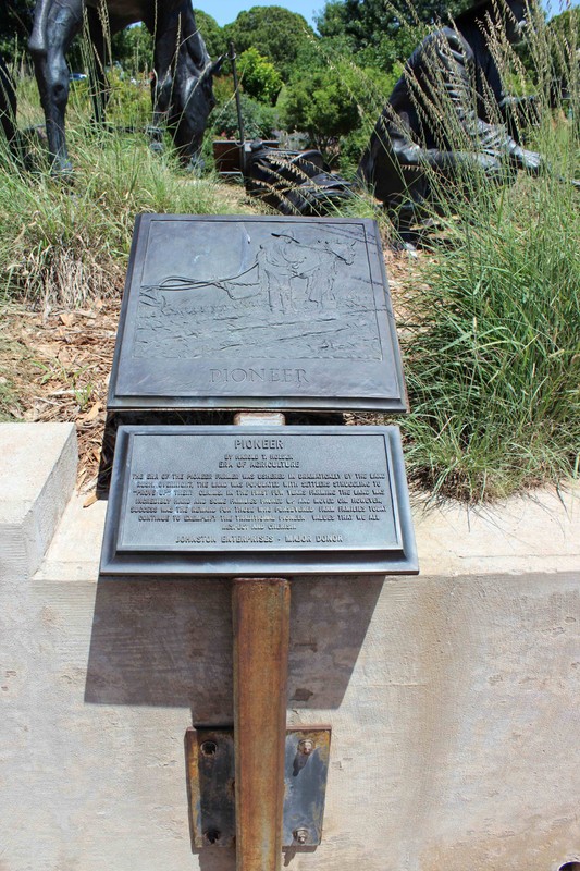 Bronze plaque with a relief image of a man driving a horse drawing a plow. Another plaque below it has text explaining the image.