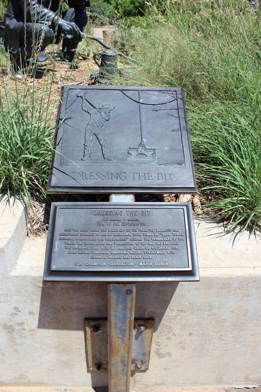 Bronze plaque with a relief image of a man driving a horse drawing a plow. Another plaque below it has text explaining the image.