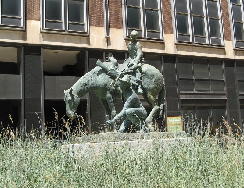 Bronze statue of boy on horseback; a man kneels in front of them, driving a stake into the ground.