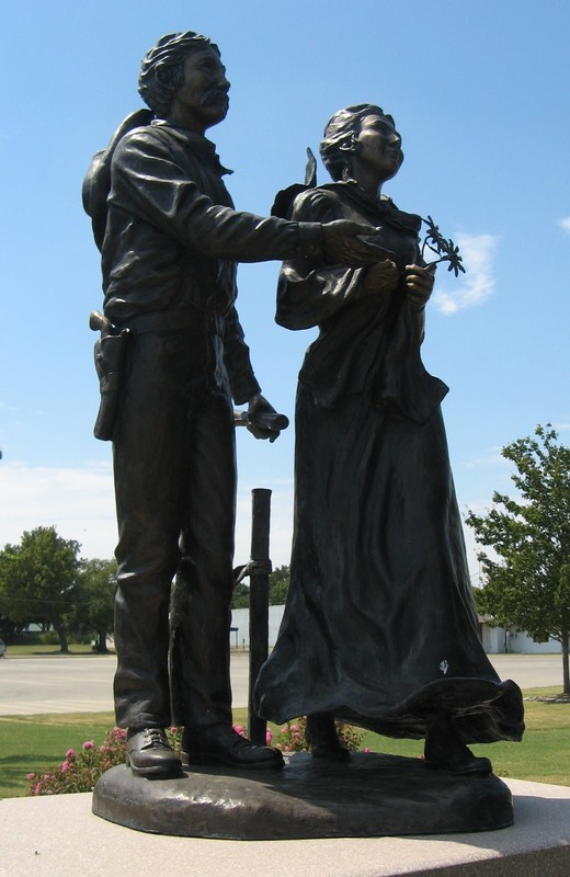 Bronze statue of a standing man and woman. A claim stake stands behind them.