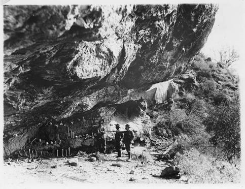 Black and white photo, late 1890s possibly, of men documenting battle. Visible are the skeletal remains of the dead from the battle