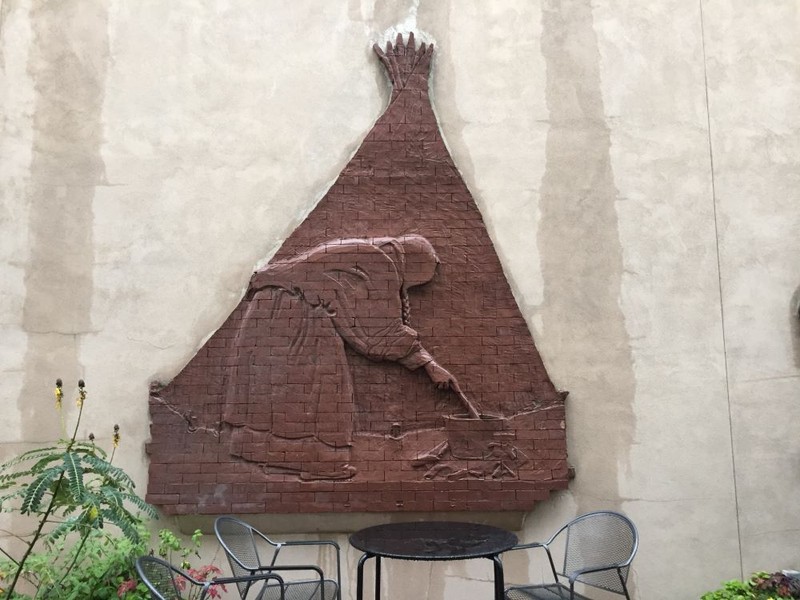 Brick relief of a woman leaning over a fire in front of a tipi