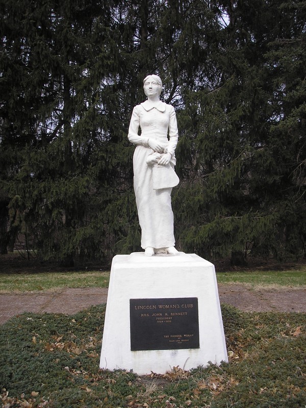 White statue of a woman in a long dress holding a pocketbook