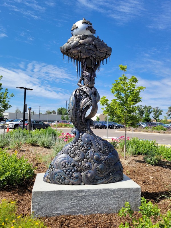 Photo of metal sculpture of human form with a dripping raincloud and silver colored orb on top