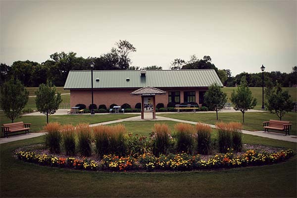 Planter filled with flowers in foreground. Warming house building with green metal roof in background.