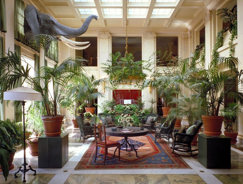 The conservatory is two stories tall and features ceiling windows and numerous plants.