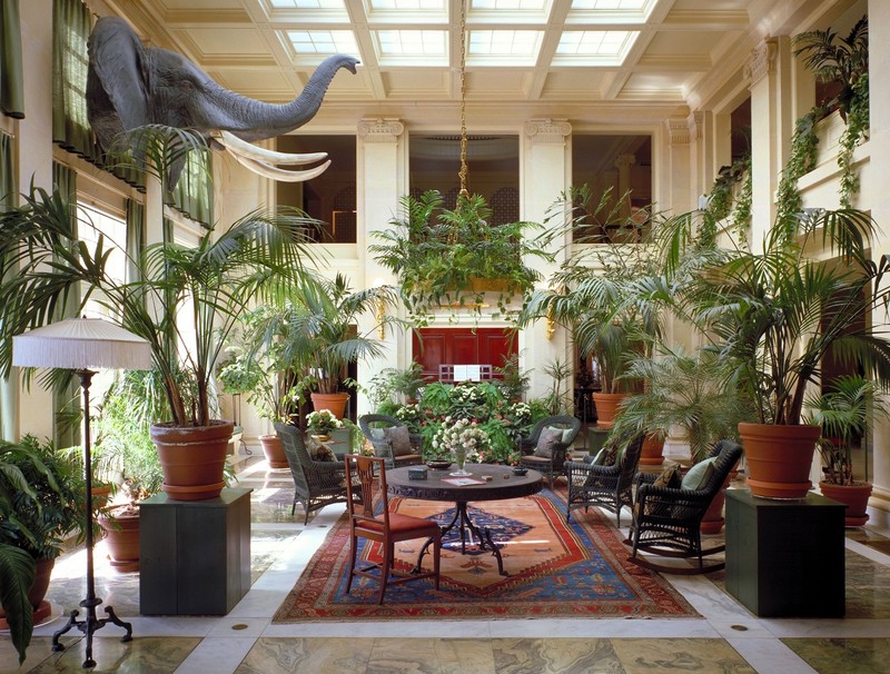 The conservatory is two stories tall and features ceiling windows and numerous plants. 