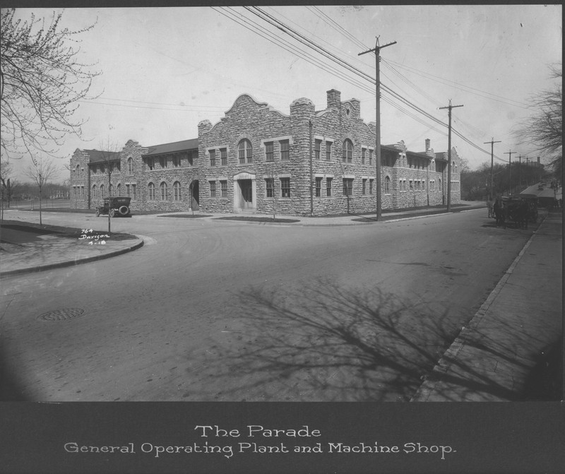 A picture of a two-story Mission Revival -style limestone building. A caption at the bottom of the image reads "THE PARADE   General Operating Plant and Machine Shop"