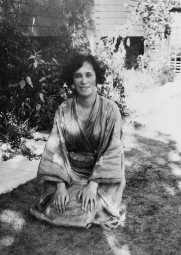 Black and white image of woman in Japanese dress sitting on grass in front of house