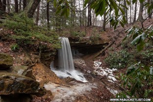 water fall from a distance view, showing the water rushing off the side of the rocks creating a tall skinny waterfall