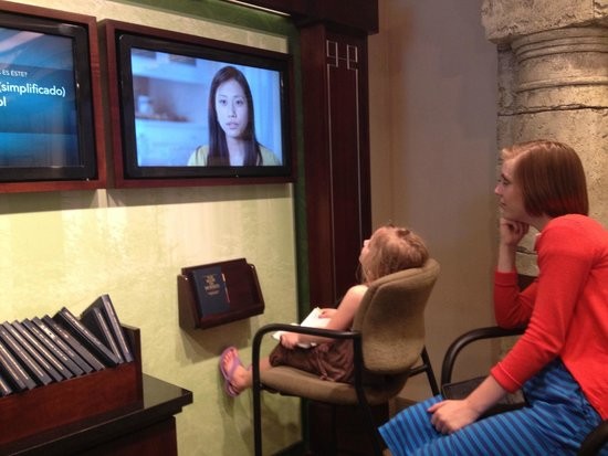 Two visitors watch a film about the Book of Mormon in visitors center