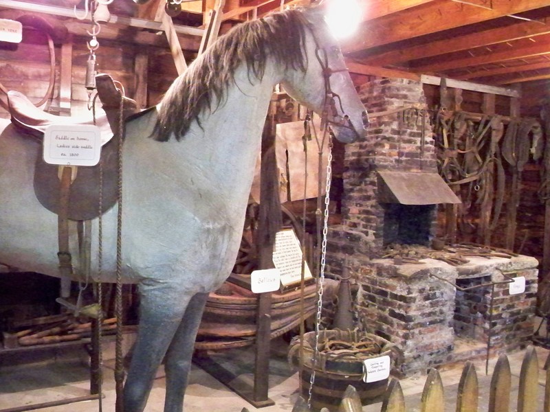 A Blacksmith forge and bellows are in the background of a paper-mâché horse that would have sat in front of the shop to symbolize the Blacksmith shop for any illiterate patrons.