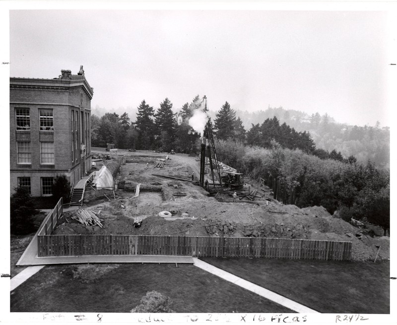  Black and white photograph showing construction of the Medical Research Building on the Marquam Hill campus of the University of Oregon Medical School. A crane and excavated earth are visible on a hillside with trees in the background.