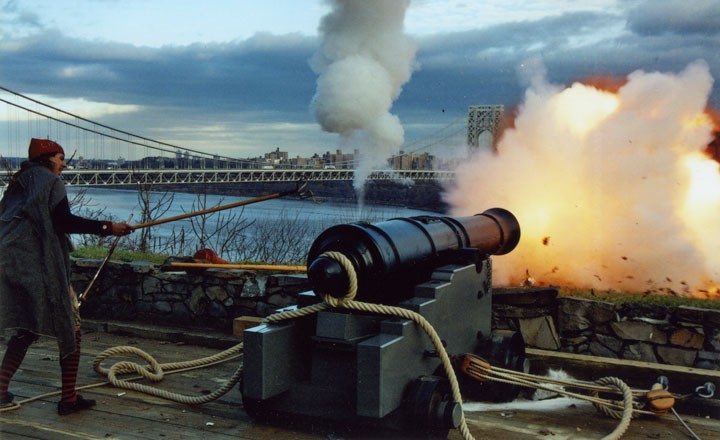 A canon is fired during a reenactment at the museum. The George Washington Bridge is in the background.