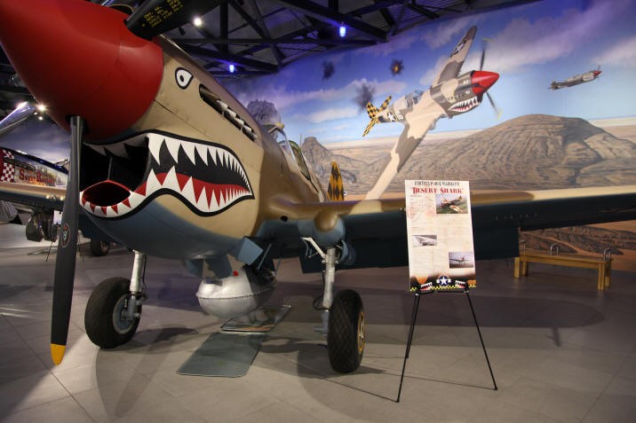 A fighter plane on display in font of a mural depicting in the sky