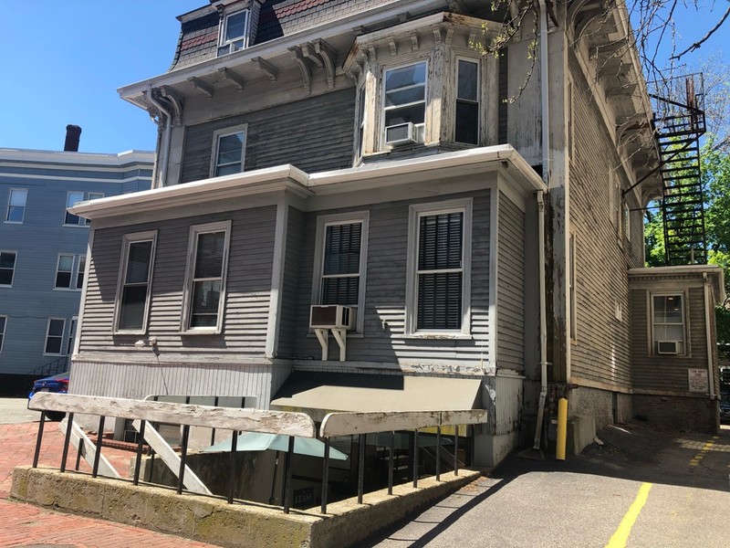 Color photo of a house with gray wood panelling. 