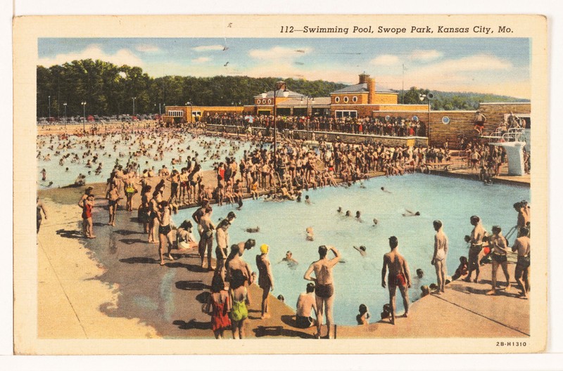 A printed color image showing a view of a crowded pool complex. Numerous people are in the water, with additional crowds on the edge. In the background, a building is visible as part of the complex.