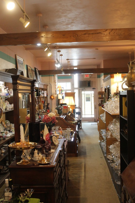 A bright showroom, with the glass rear door at center. The space is narrow and deep. Many glassware items are displayed for sale.