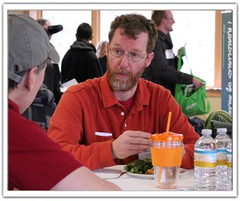 Two men sitting at a table eating food and talking