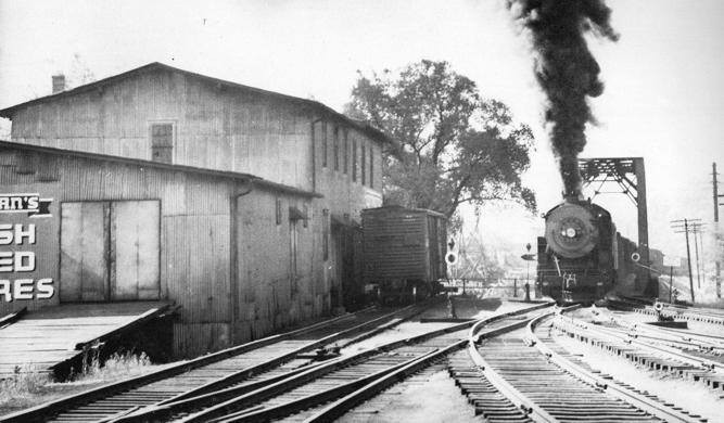 A black and white photo shows the backside of the mill, which abuts railroad tracks.