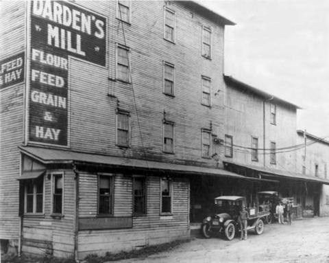 A black and white photo of a four-story building with a historic car parked out front.
