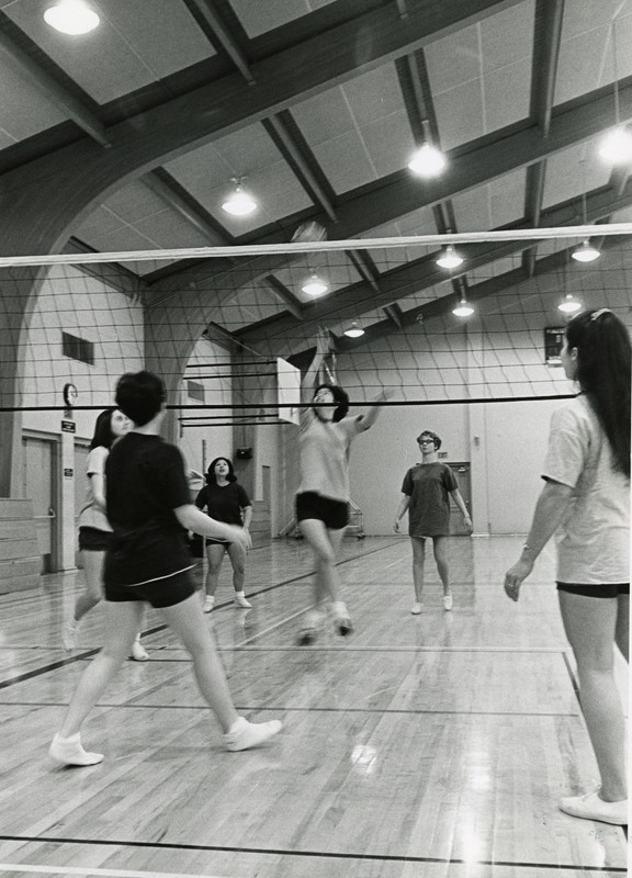 Black and white photograph of women playing volleyball on an indoor court.