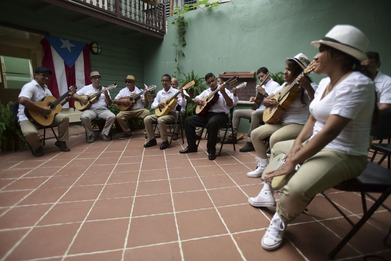 A group of musicians playing instruments like: cuatro, guitars, and traditional drums