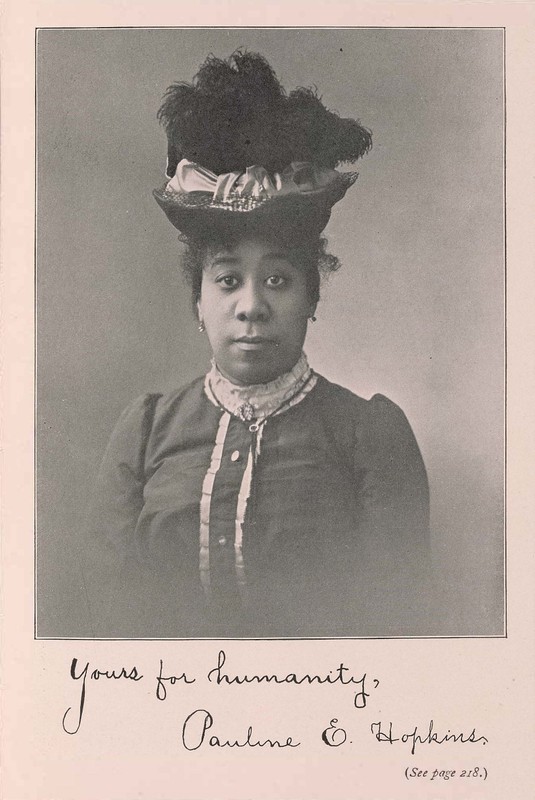 A straight-on black and white portrait of a black woman who is wearing a tall hat made of feathers