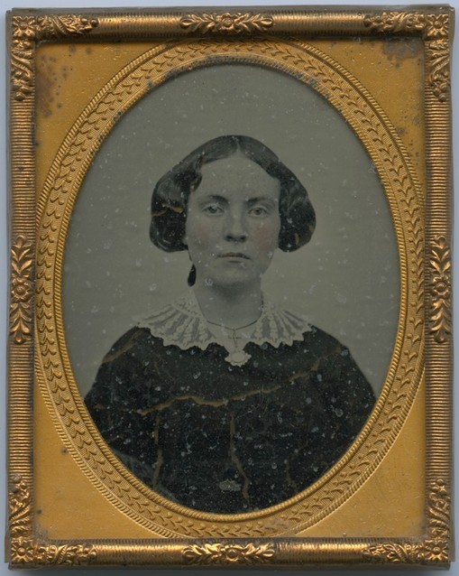 Black & White photo portrait of a dark-haired woman in a black dress, with a white lace collar. In a gold oval frame.
