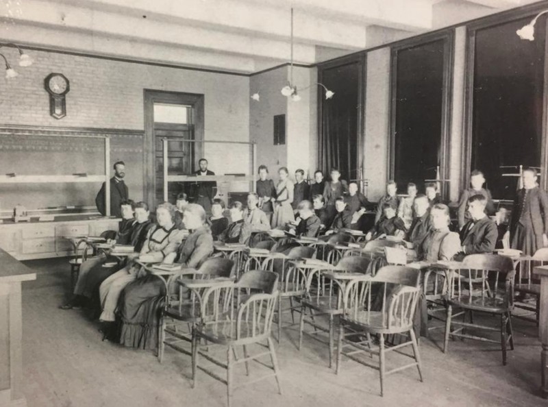 A black and white photo of white students sitting at desks in a classroom