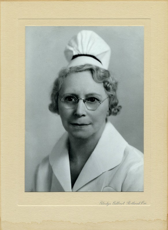 A black & white photograph of Emma Jones, R.N. She is an older woman with pin-curled gray hair, a nurse's uniform, wire-rimmed glasses, and a nurse's cap from her nursing school.