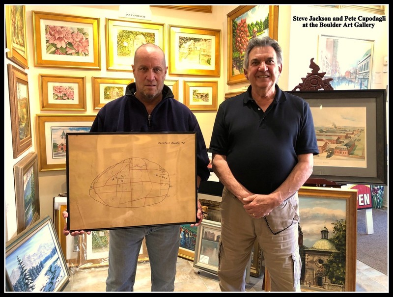 An image of two men, Steve Jackson and Peter Capodagli, one holding a drawing of plans to reconstruct the rollstone boulder.  Behind them is the Boulder Art Gallery.  