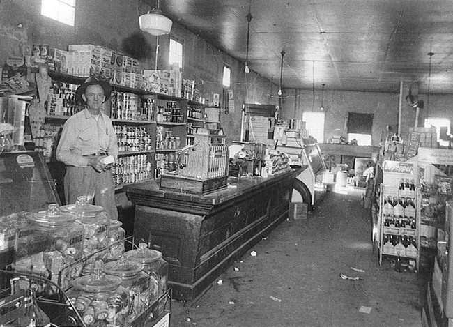 A black and white photo of a young man standing instead a store.