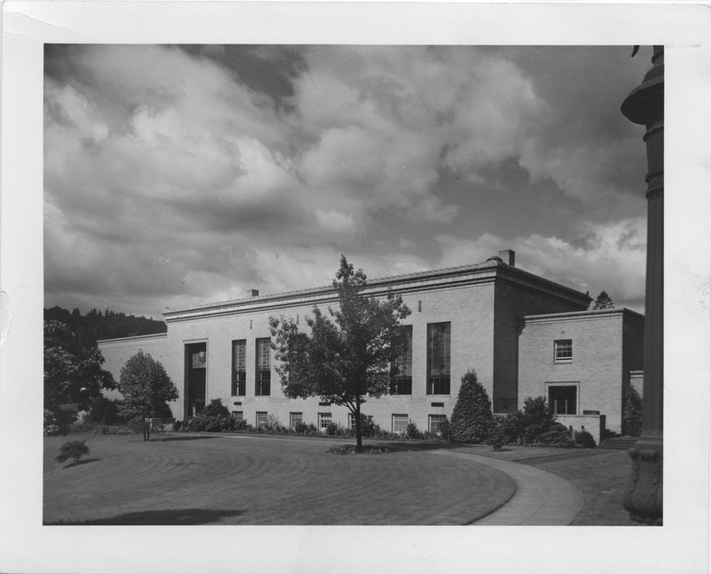 Black and white photograph of the Old Library building, framed by clouds and several young trees. Image taken facing southwest.