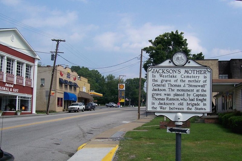 The historical marker is located between a commercial and a residential area in Ansted