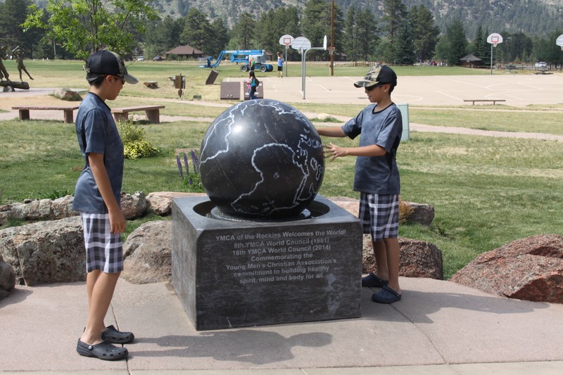 This image shows the globe shortly after its installation. The globe is dark gray with light outlines of the continents. It rotates in a small pool of water as children interact with it. 