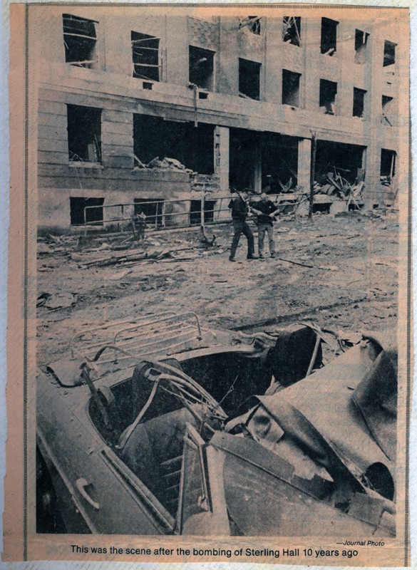 Newspaper clipping printed 10 years after the bombing at Sterling Hall. The image features the wreckage at Sterling Hall, showing two men standing amongst debris, and a car in the front of the image, also filled with debris.  