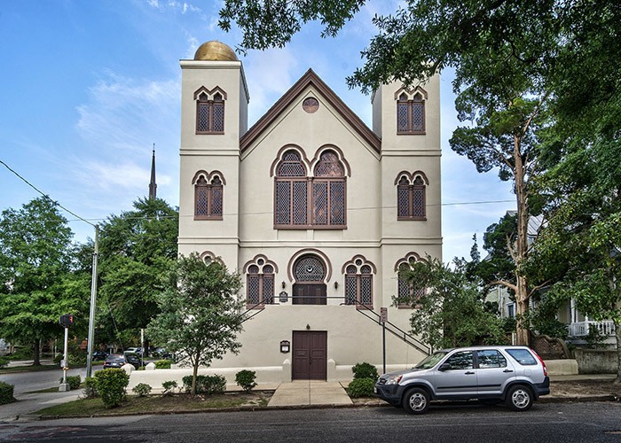 A Moorish-revival synagogue sits on a street corner. A gold onion-dome tops each of the two, three-story towers.