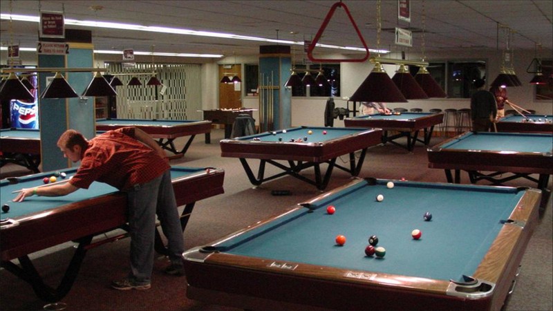 Man shooting pool in a room with 6 pool tables